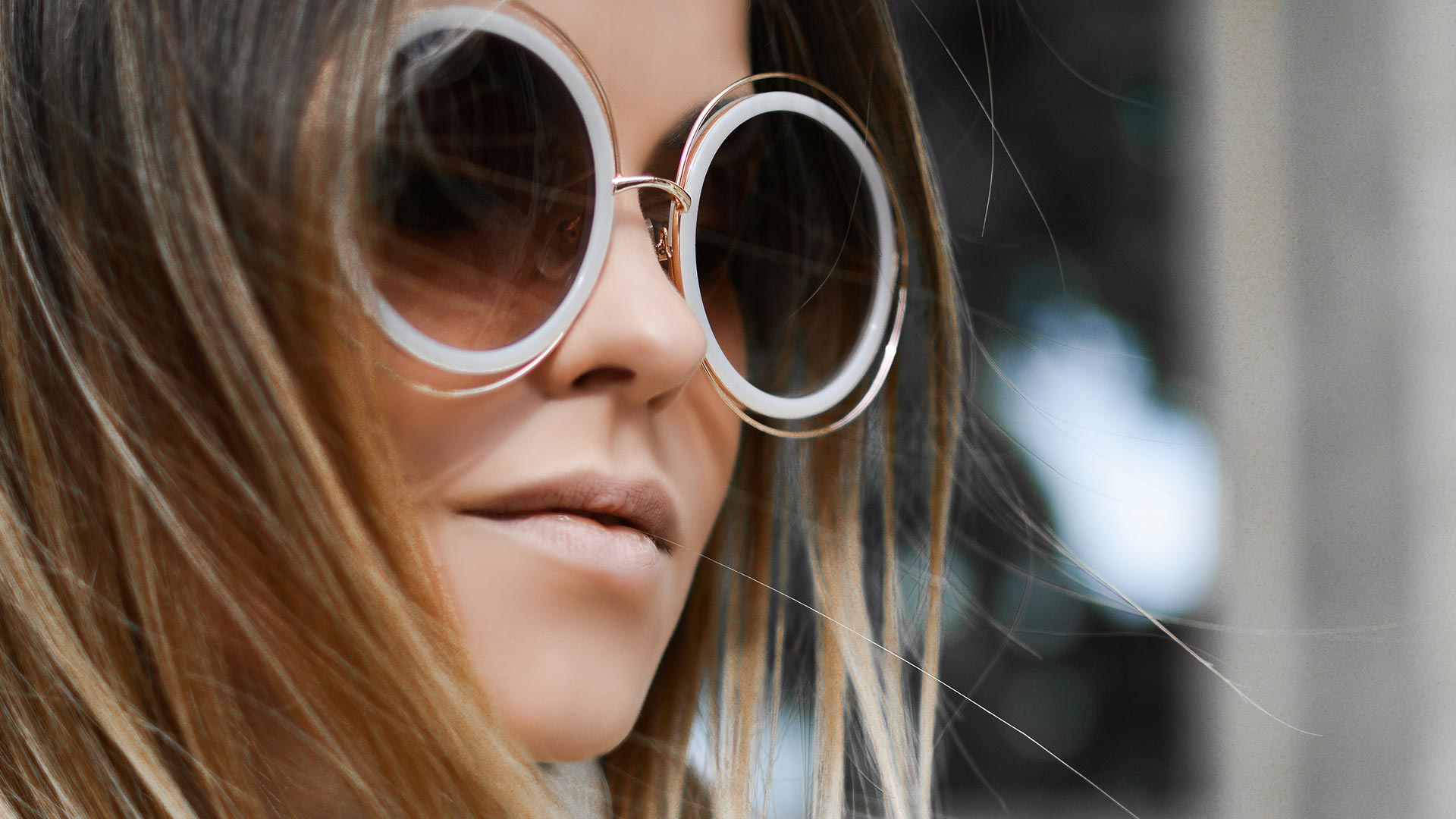 Frau mit Ombré-Haar trägt übergroße runde Sonnenbrillen mit weißen Ringen und braunen Gläsern – modische Urlaubsbrillen bei Seitz Optik Limburg