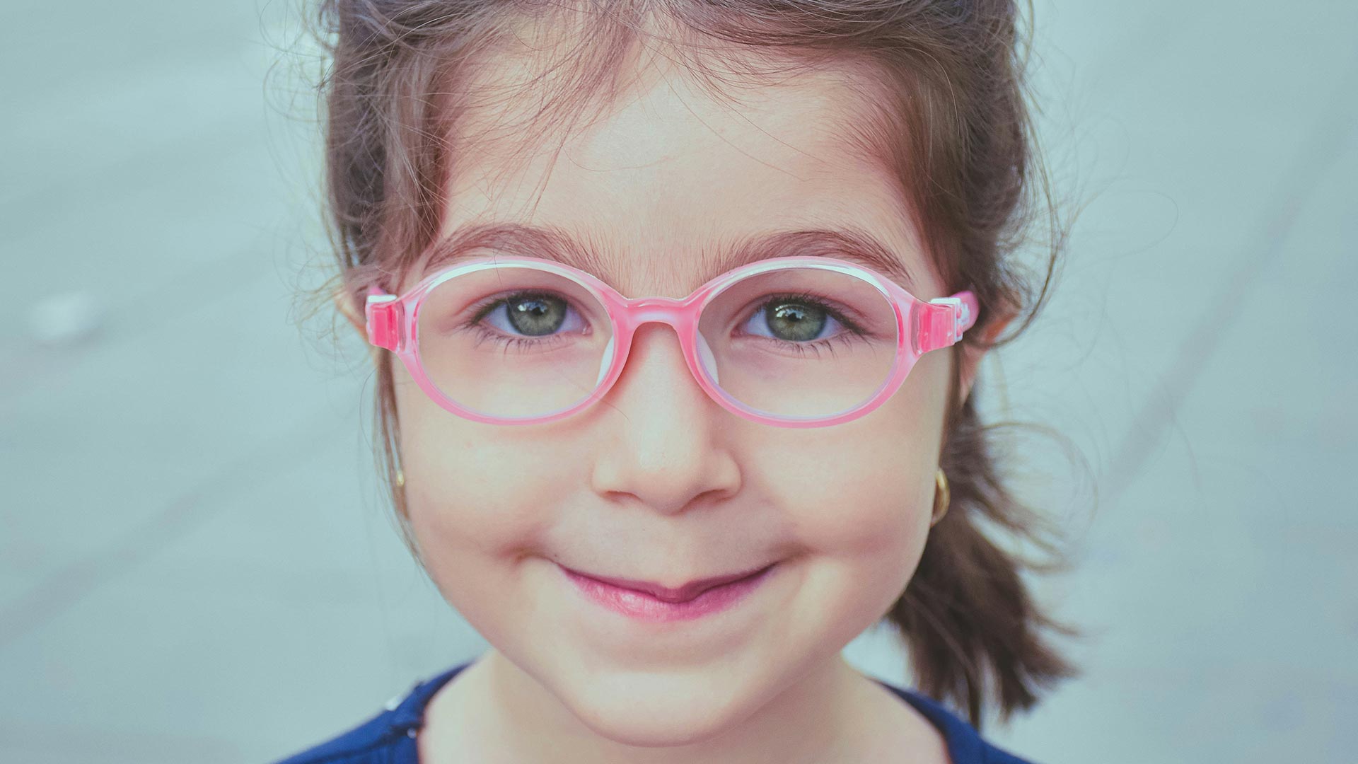 Fröhlich lächelndes Mädchen mit pinker Kinderbrille mit flexiblen Bügeln – passende und sichere Kinderbrillen bei Seitz Optik in Limburg