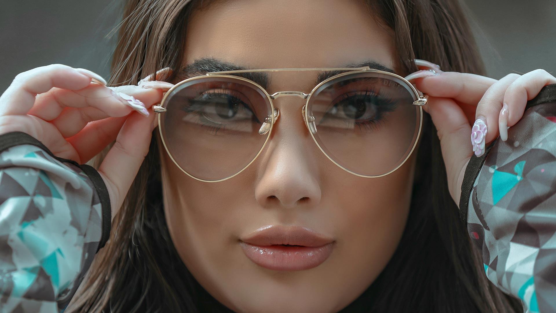 Junge Frau hält sich eine goldene Pilotenbrille mit getönten Gläsern ans Gesicht und schaut direkt in die Kamera – Brillen für jedes Alter bei Seitz Optik Limburg