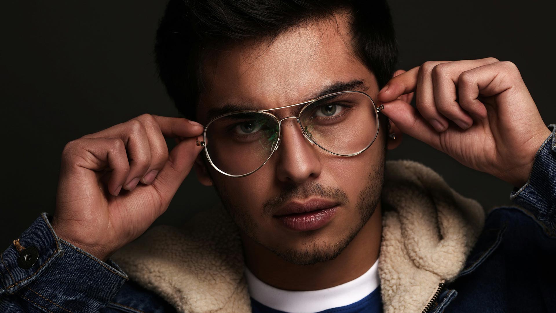 Junger Mann setzt sich eine silberne Aviator-Brille auf und schaut direkt in die Kamera – stylische Brillen für jeden Typ bei Seitz Optik in Limburg